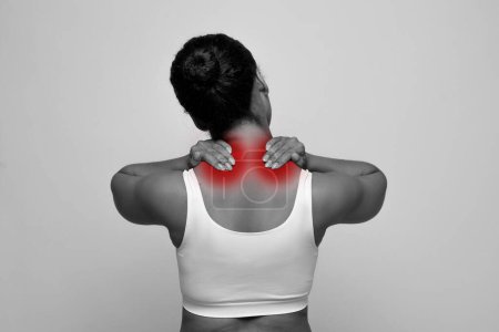 Foto de Foto monocromática de la mujer afroamericana en la parte superior blanca que masajea el cuello, frotando las manchas rojas doloridas en la parte superior de la espalda, aislado en el fondo, que sufre de tensión muscular - Imagen libre de derechos