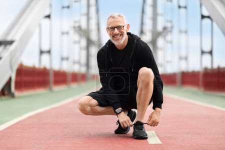Photo for Photo of cheerful self-confident grandpa senior man fixing shoelaces new quality sneakers while running by urban town outside. Elderly sportsman exercising outdoor, copy space - Royalty Free Image