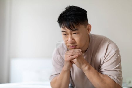 Photo for Closeup of depressed unhappy upset chinese middle aged man sitting on bed at home. Asian man feeling lonely, experiencing breakup or divorce. Anxiety, mental disorder, copy space - Royalty Free Image