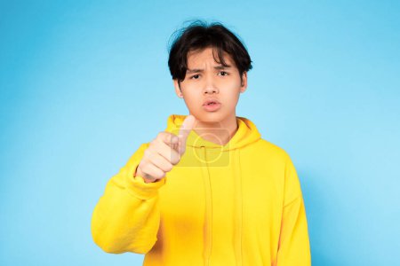 Téléchargez les photos : Salut toi. Japonais mécontent adolescent Guy pointant doigt à la caméra, argumentant et exprimant des émotions négatives posant sur fond bleu. Studio Shot. Vous avez fait un mauvais choix concept - en image libre de droit