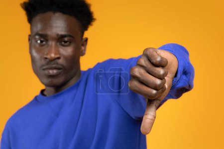Photo for I dont like it. Sad disappointed young black man showing thumb down, looking at camera isolated on yellow studio background, selective focus on guy hand. Negative opinion, dislike - Royalty Free Image