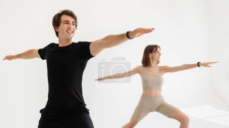 Téléchargez les photos : Heureux jeune homme et femme européens en vêtements de sport exercice pour les mains, pratiquer le yoga dans la salle de gym, à la maison, isolé sur fond clair, panorama. Soins corporels, mode de vie actif, sport et fitness - en image libre de droit
