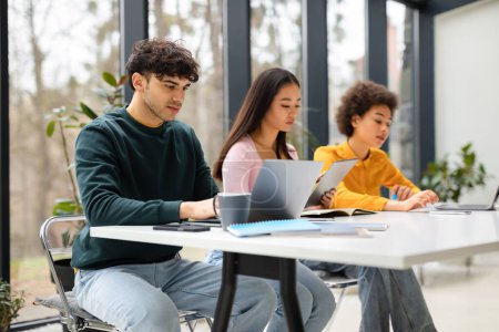 Photo for Diverse group of students sitting in university library with books and technology learning for exams, multiracial guy and ladies making online research indoors - Royalty Free Image
