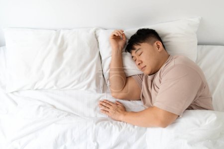 Photo for Top view of peaceful handsome middle aged asian man wearing pajamas sleeping alone in his huge comfy bed, empty space next to him. Being single, solo lifestyle concept - Royalty Free Image