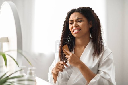 Photo for Young Black Woman Irritated By Tangled Hair, Using Bamboo Brush At Home, Unhappy African American Female Suffering Painful Feeling, Frowning While Combing Her Curly Hair, Copy Space - Royalty Free Image