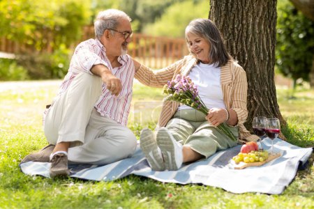 Photo for Glad senior european man gives bouquet to woman, enjoy romantic date, picnic and lunch in park, outdoor. Weekends, holidays, love and relationships, food and vine for dinner - Royalty Free Image
