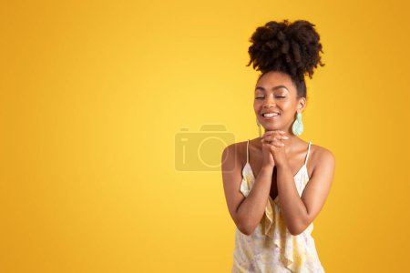 Téléchargez les photos : Heureuse femme afro-américaine millénaire en robe faisant geste de prière, souhait et espoir, isolée sur fond jaune, studio. Rêve, mode de vie, bonnes nouvelles, publicité et offre, gratitude - en image libre de droit