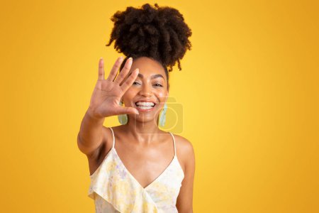 Foto de Riendo milenaria dama afroamericana extendiendo la mano a la cámara, sin tomar fotos signo, aislado en el fondo amarillo, estudio. Detener el gesto, emociones divertidas, redes sociales, anuncios y ofertas - Imagen libre de derechos