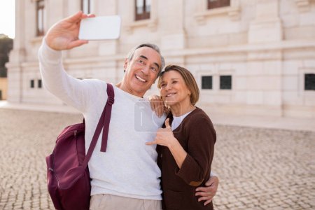 Téléchargez les photos : Senior Globetrotters. Happy Mature Travelers Conjoints Snapping Selfies Via Smartphone Poser tout en visitant Lisbonne à l'extérieur, Poser en tenue décontractée avec sac à dos. Focus sélectif - en image libre de droit