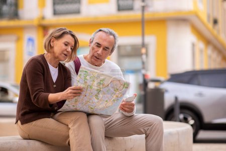 Photo for Vacation Destination. European Mature Tourists Couple With Smartphone And Touristic Map Planning Their Holidays Sitting Outdoor In Urban Area. Free Space For Advertisement Text - Royalty Free Image