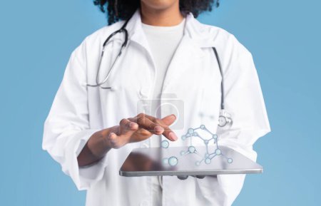Téléchargez les photos : Jeune femme noire médecin thérapeute en manteau blanc utilise une tablette avec écran blanc et des molécules, isolé sur fond bleu studio, collage. App pour les soins médicaux, les soins de santé, site web scientifique - en image libre de droit