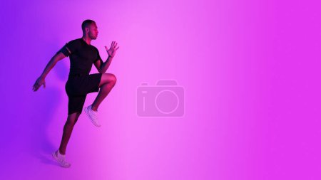 Photo for Black Athlete Guy Jumping Exercising During Training On Purple Neon Studio Background, Looking Aside At Copy Space. Full Length, Side View Shot. Male Fitness Workout And Sport Motivation. Panorama - Royalty Free Image