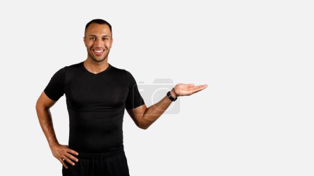Téléchargez les photos : Offre fitness. Fit afro-américain jeune homme en Fitwear Gesturing avec la main montrant l'espace vide pour le texte, la publicité du produit sportif et souriant à la caméra debout sur fond blanc. Panorama - en image libre de droit