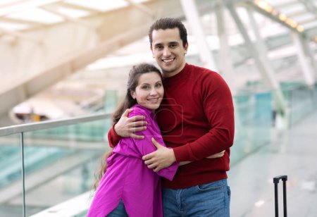Téléchargez les photos : Bon voyage. Jeune couple romantique de touristes embrassant la pose à l'aéroport moderne, souriant à la caméra. Homme et femme debout avec valise et câlins, heureux de voyage vacances - en image libre de droit
