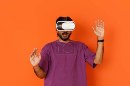 Photo for Modern technologies and entertainment concept. Excited dark-skinned young man in casual using virtual reality headset, gesturing and grimacing, playing video games, isolated on orange - Royalty Free Image