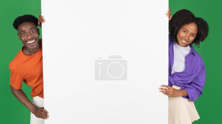 Photo for Smiling millennial african american couple in casual with big banner with blank space, isolated on green studio background, panorama. Recommendation together, people emotions, sale, ad and offer - Royalty Free Image