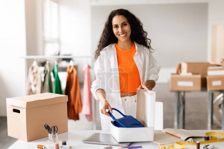 Photo for Clothing Designer Woman Smiling To Camera While Packing Handbag, Preparing Parcel Boxes For Delivery, Posing In Modern Online Fashion Store Indoor. Clothes Retail Business Success Concept - Royalty Free Image