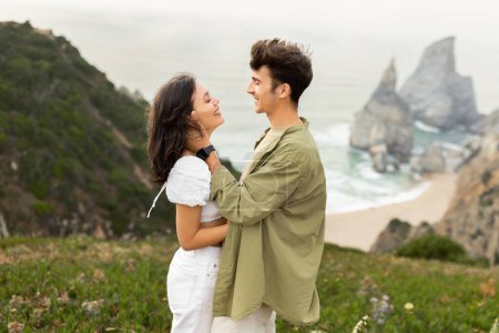 Téléchargez les photos : Sérénité au bord de la mer. Couple européen amoureux profitant d'un rendez-vous romantique et collant sur une falaise rocheuse avec belle vue sur l'océan, vue latérale, espace libre - en image libre de droit