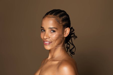 Photo for Portrait of smiling black middle aged woman with naked shoulders posing over brown studio background and looking at camera. Happy nude female with glowing perfect skin - Royalty Free Image