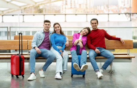 Photo for Group Of Four Travelers Friends Sitting With Suitcases Waiting For Flight Posing At Modern Airport Departure Terminal, Smiling At Camera. Two Romantic Couples Travelling Together - Royalty Free Image