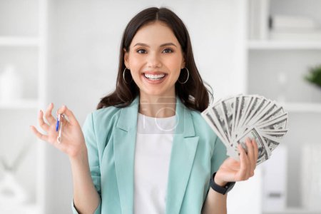 Photo for Happy young european woman in suit shows keys and lot of money in modern office interior. Businesswoman and successful business, job, real estate, purchase house and mortgage, loan - Royalty Free Image