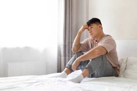Photo for Depressed unhappy upset chinese middle aged man sitting on bed at home, looking at copy space. Asian man feeling lonely, experiencing breakup or divorce. Anxiety, mental disorder - Royalty Free Image