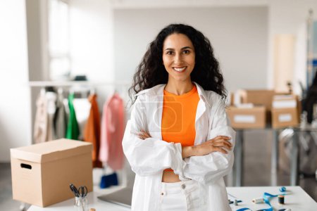 Photo for Professional Clothing Designer Woman Standing With Folded Hands At Modern Fashion Design Studio Interior, Smiling To Camera. Small Business, Boutique Ownership And Entrepreneurship - Royalty Free Image
