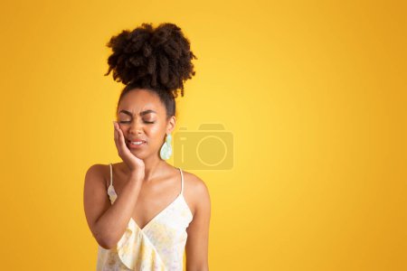 Photo for Despaired young black woman with closed eyes presses hand to cheek, suffering from toothache, isolated on yellow background, studio. Health problems, dentistry care, medicine help - Royalty Free Image