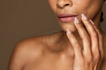 Téléchargez les photos : Gros plan de femme noire avec une peau impeccable touchant les lèvres avec les doigts posant sur fond brun studio, recadré. Dame méconnaissable appréciant la routine d'auto-soins - en image libre de droit
