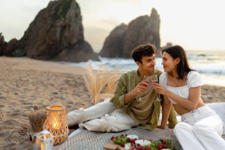 Téléchargez les photos : Des clinks côtiers. Jeune couple romantique ayant pique-nique sur la plage de sable fin au bord de l'océan, gars et dame boire du vin et profiter de la date à la côte, espace libre - en image libre de droit