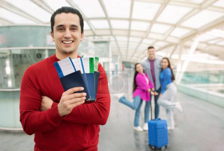 Photo for Great Travel Offer. Tourist Man Showing Passports And Boarding Passes Posing With Group Of Friends At Airport Indoor. Tour Agent Advertising Transportation Service. Selective Focus - Royalty Free Image