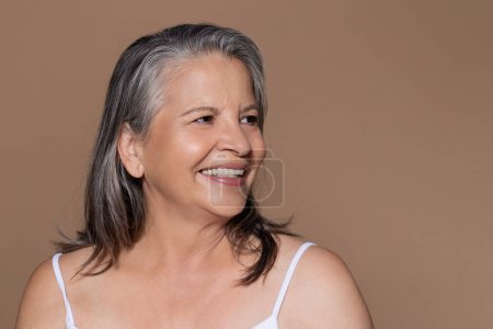 Photo for Positive senior caucasian lady with gray hair enjoy anti-aging treatment looking at blank space, isolated on brown background, studio. Spa procedures, beauty care, fighting and cosmetics - Royalty Free Image