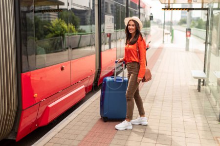 Photo for Transportation. Cheerful Tourist Woman With Suitcase Getting On A Modern Tram At Station Outdoor. Contented Passenger Commuting Via Public Transport In City. Full Length Shot - Royalty Free Image