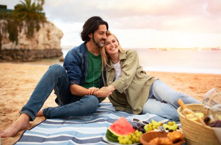 Photo for Happy romantic couple relaxing together on outdoor picnic at beach, young millennial man and woman embracing and smiling, spending time on ocean shore, enjoying date or honeymoon vacation, copy space - Royalty Free Image