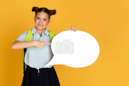 Téléchargez les photos : Joyeux adolescent fille européenne avec sac à dos pointe du doigt le nuage abstrait pour les mots et les pensées, isolé sur fond de studio jaune. Recommandation étude, éducation à l'école - en image libre de droit