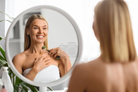 Photo for Anti-Aging Skincare. Smiling Mature Woman Massaging Neck Skin With Greenstone Jade Roller Tool, Portrait Of Attractive Middle Aged Lady Making Beauty Treatments At Home, Selective Focus - Royalty Free Image