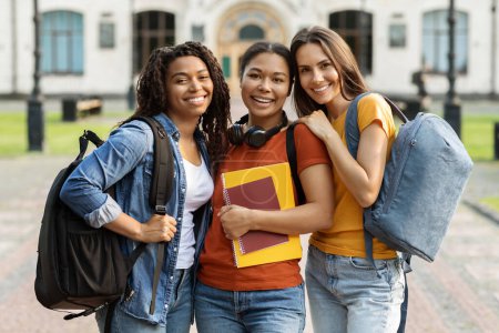 Photo for College Friendship Concept. Three Multiethnic Female Students Posing Outdoors At Campus, Cheerful Young Muticultural Friends With Backpacks And Workbooks Embracing And Smiling At Camera, Closeup - Royalty Free Image