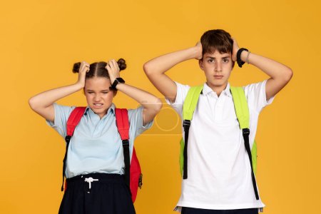 Photo for Sad angry tired teen european boy and girl with backpacks cover ears with hands, isolated on yellow studio background. Friendship, childhood, problems in education at school, bullying, noise - Royalty Free Image