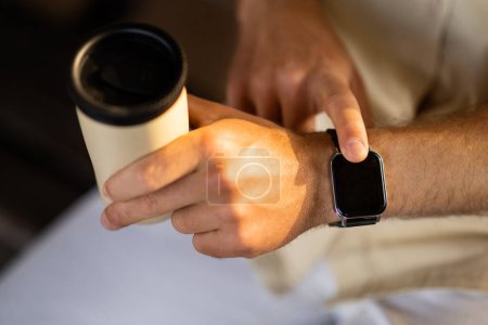 Photo for Close up shot of a businessman hand that uses a smart watch to view incoming messages and calls while sitting outdoors and drinking takeaway coffee, the gadget simplifies his life, cropped - Royalty Free Image