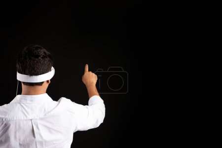 Téléchargez les photos : Vue arrière d'un homme d'affaires portant des lunettes de réalité virtuelle, pointant du doigt et touchant un écran vierge invisible sur fond noir, espace libre, maquette - en image libre de droit
