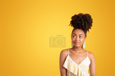 Foto de Sonriente joven negro rizado dama en vestido se ve en el espacio de copia, disfruta de vacaciones, gran venta, aislado en el fondo amarillo, estudio. Estilo de vida de moda, anuncio y oferta, cuidado de belleza - Imagen libre de derechos