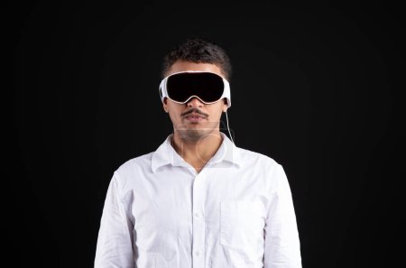 Photo for Portrait of serious brazilian man in shirt posing in VR vision pro glasses over black studio background. Young generation choose virtual reality relaxation concept - Royalty Free Image
