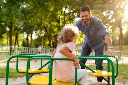 Photo for Child girl having fun with her father on outdoor playground, dad riding daughter on carousel, spending active leisure time together. Happy parenthood and childhood - Royalty Free Image