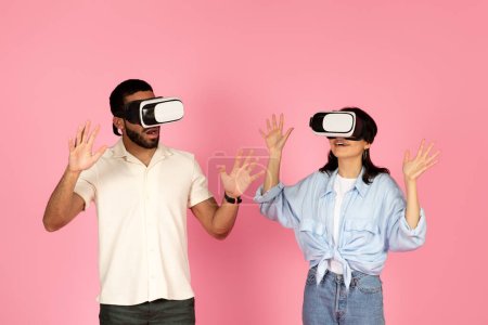 Photo for Surprised millennial guy and woman using VR glasses and gesturing, young couple enjoy play game in virtual reality, isolated on pink background, studio. Fun, entertainment with technology - Royalty Free Image