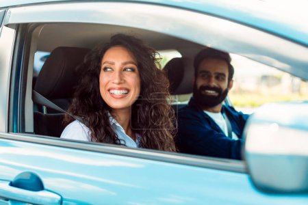 Photo for Enjoy family journey. Arab man driving car, focus on smiling lady sitting in auto on passenger seat with open window, looking on road and smiling - Royalty Free Image