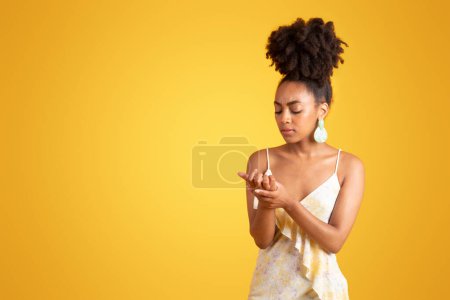 Photo for Sad young black woman looks at her hand, need new manicure, suffers from pain and injury, isolated on yellow background, studio. Health problems, nails care, ad and offer, beauty care - Royalty Free Image