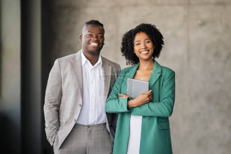 Téléchargez les photos : Partenariat d'affaires. Coworkers afro-américains joyeux paire posant avec tablette numérique debout et souriant regardant la caméra au bureau, portant des tenues formelles. Carrière réussie, Emploi - en image libre de droit