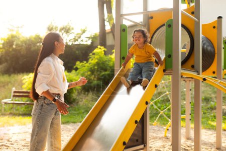 Photo for Adorable Joyful Korean Baby Girl Riding Down The Slides At Playground With Mommy, Woman Looking At Little Daughter While Child Enjoying Time At Amusement Park Outside. Weekend Fun With Mom Concept - Royalty Free Image
