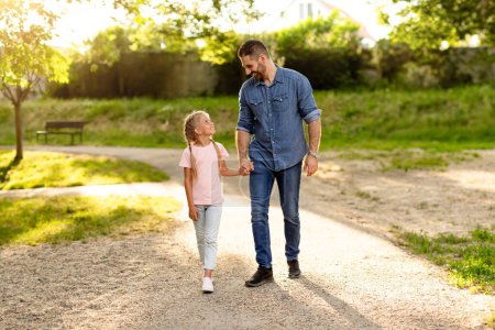 Photo for Happy family dad and daughter holding hands while walking in park, dad spending free time with his beloved child. Family, health and childhood - Royalty Free Image