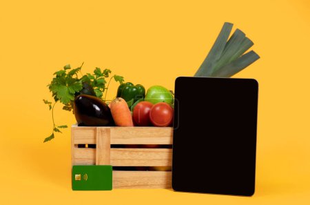 Photo for Online Grocery Shopping. Digital Tablet Computer With Empty Screen Standing Near Harvested Vegetables In Wooden Box On Yellow Studio Background. Mockup For Farm Business Advertisement - Royalty Free Image